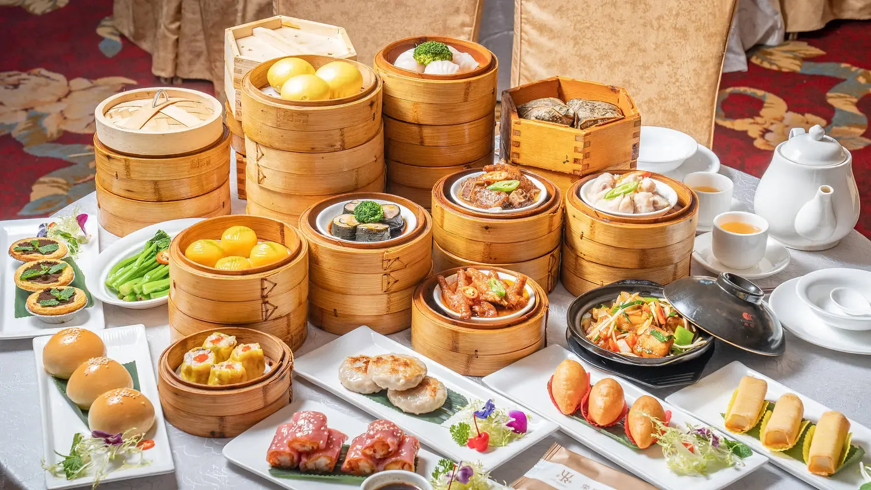 Bamboo steamers, plates of dim sum, and a teapot arranged across a dining table.