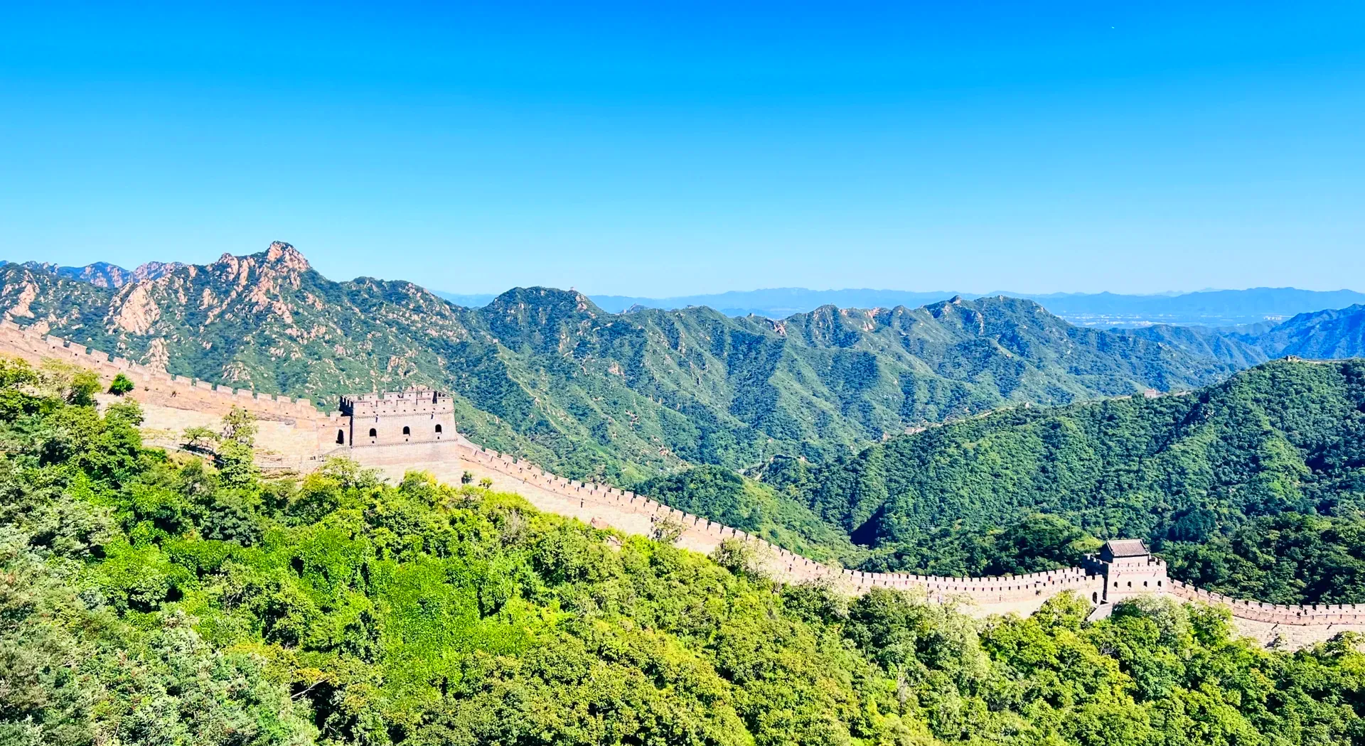 The Great Wall and watchtowers following a ridge across green mountains.