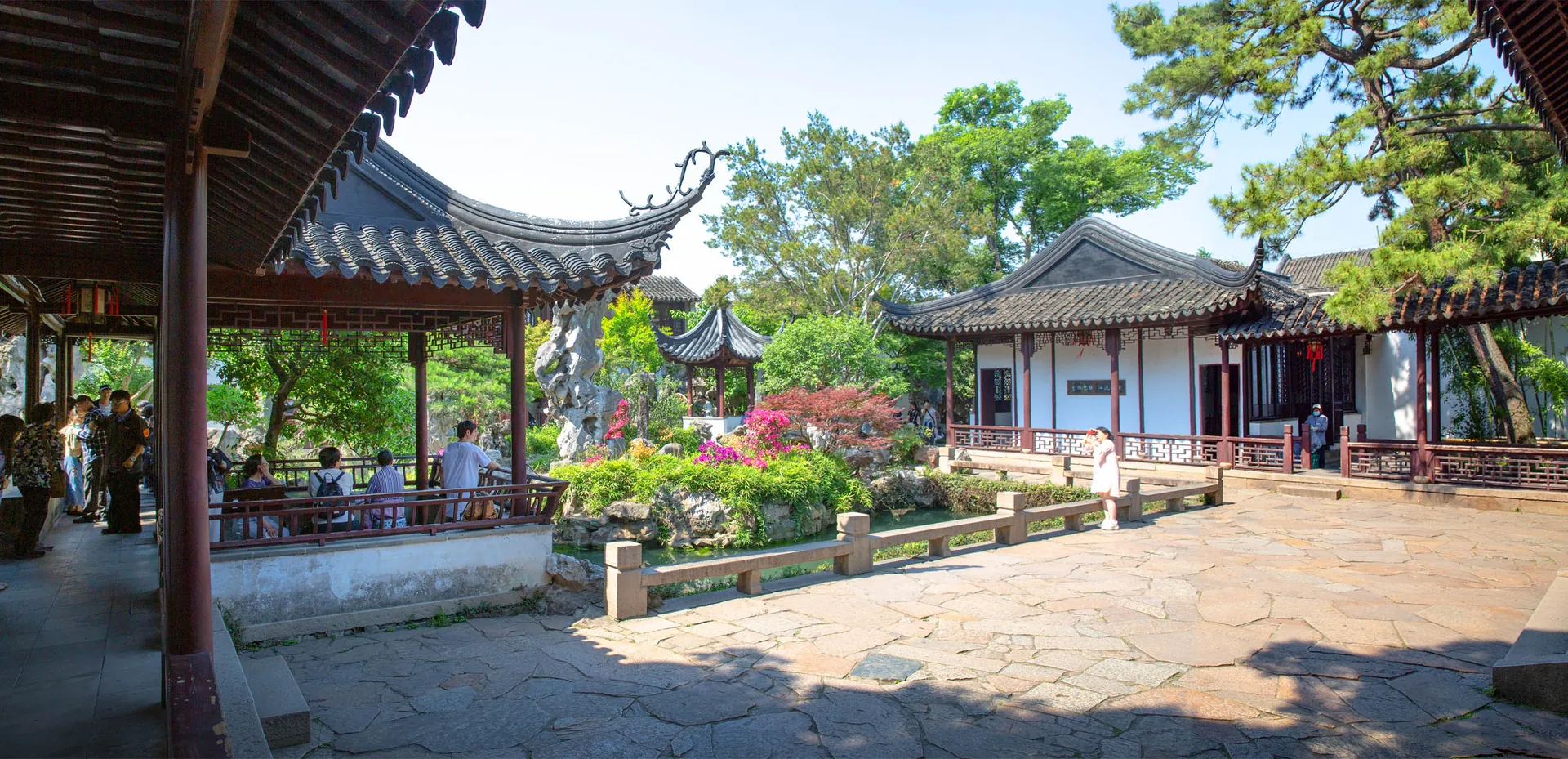 Covered walkways, tiled roofs, trees, and rocks in a classical Chinese garden.